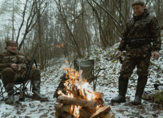 To mænd sidder rundt om bål i skov på jagt