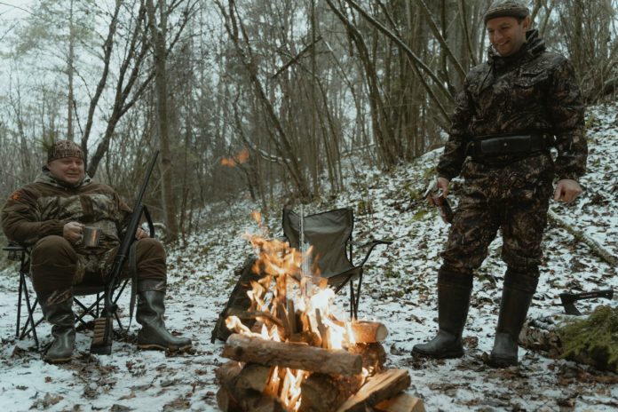 To mænd sidder rundt om bål i skov på jagt